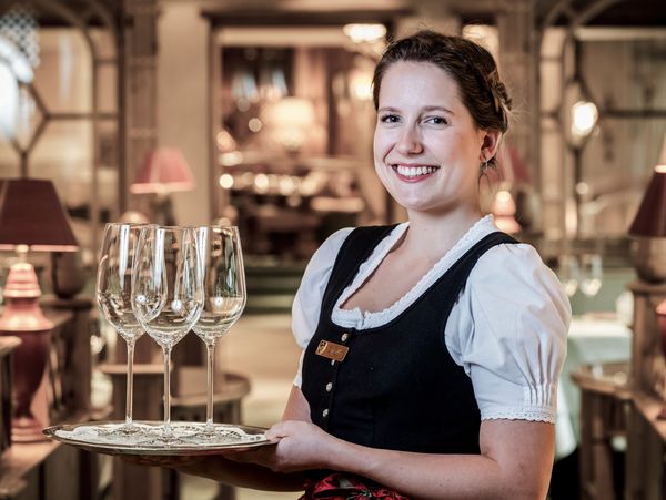Eine lächelnde Angestellte des Hotel Bareiss, welche ein Tablet mit drei Weingläsern trägt