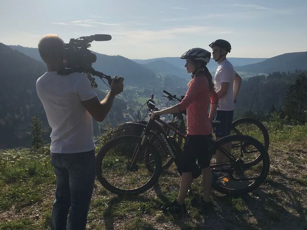Ein Kameramann filmt zwei Mountainbiker in den Bergen